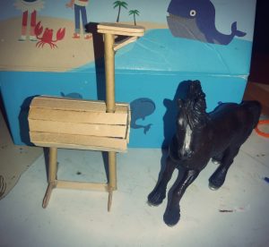 Ein schwarzes Schleichpferd steht neben einem hölzernen Pferd gebastelt aus Eisstilen 