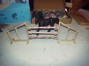 Ein dunkelbraunes Schleichpferd steht hinter einem Springhindernis gebastelt aus Eisstilen und Papier-Strohhalmen 