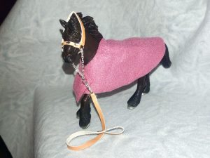 Ein dunkelbraunes Schleichpferd mit Halfter aus hellbraunem Kunstleder und einer rosanen Decke