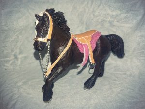 Ein dunkelbraunes Schleichpferd mit Sattel und Zaumzeug aus hellbraunem Kunstleder 