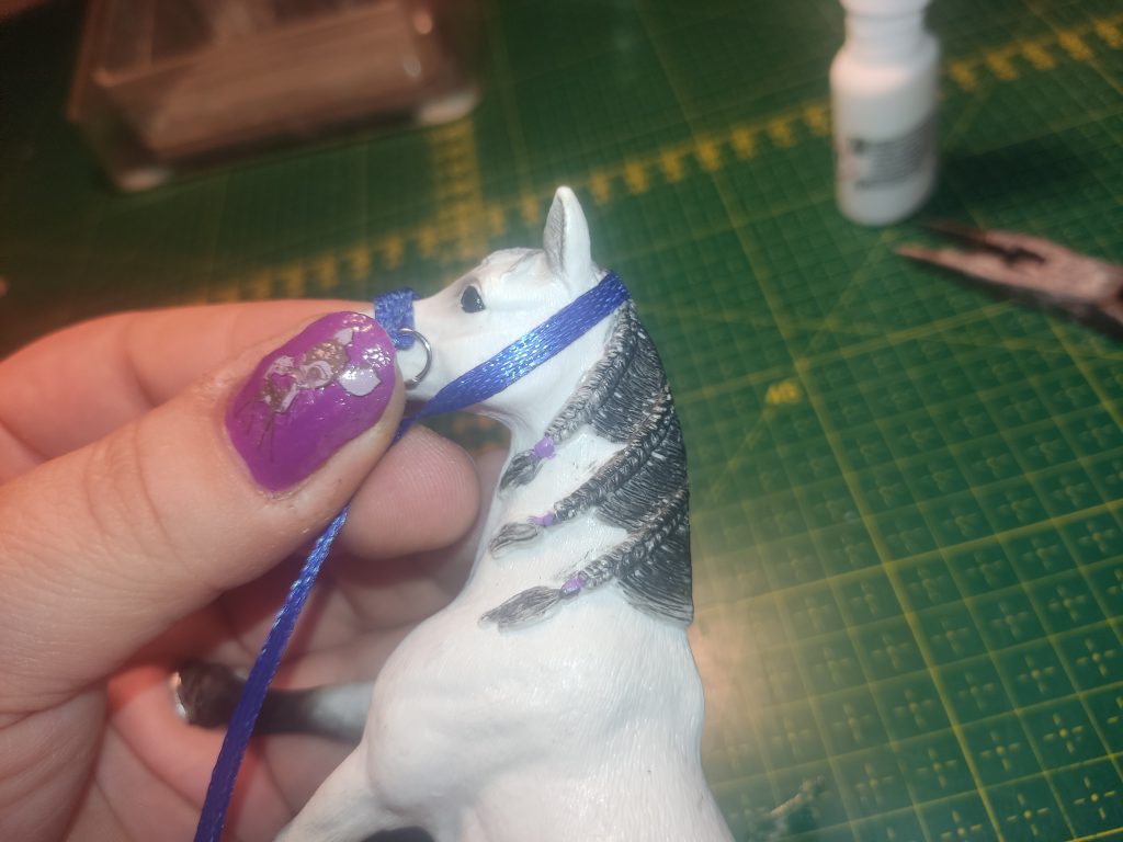 Blaues Satinband wird um den Kopf eines Schleich Schimmels gelegt