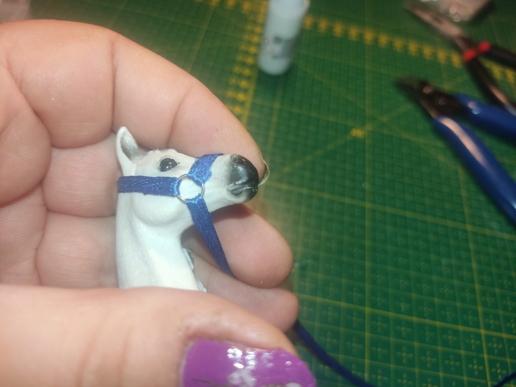 Ein Schleich Schimmelkopf in einer Hand. Darum ein blaues Halfter.